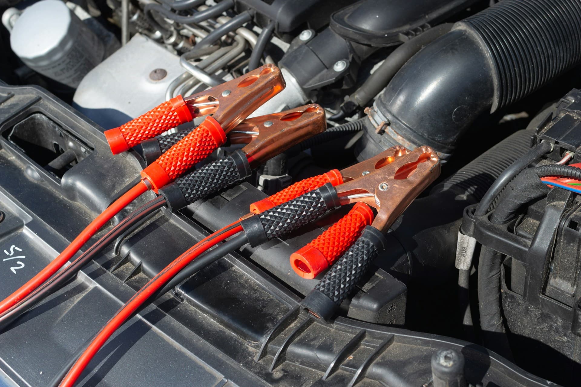 Close-up of red and black jumper cables placed on a car engine bay, used for jump-starting a vehicle.