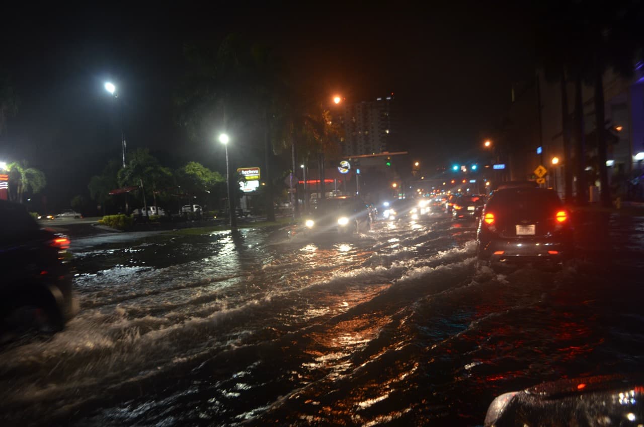 Nighttime photo of cars driving through flooded streets in Miami with headlights reflecting on the water.